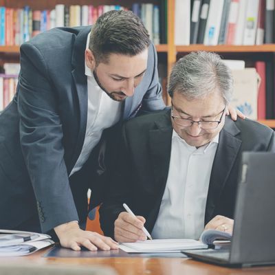 Two men at an office desk reading documents together. One man is holding a pen in preperation to sign the documents